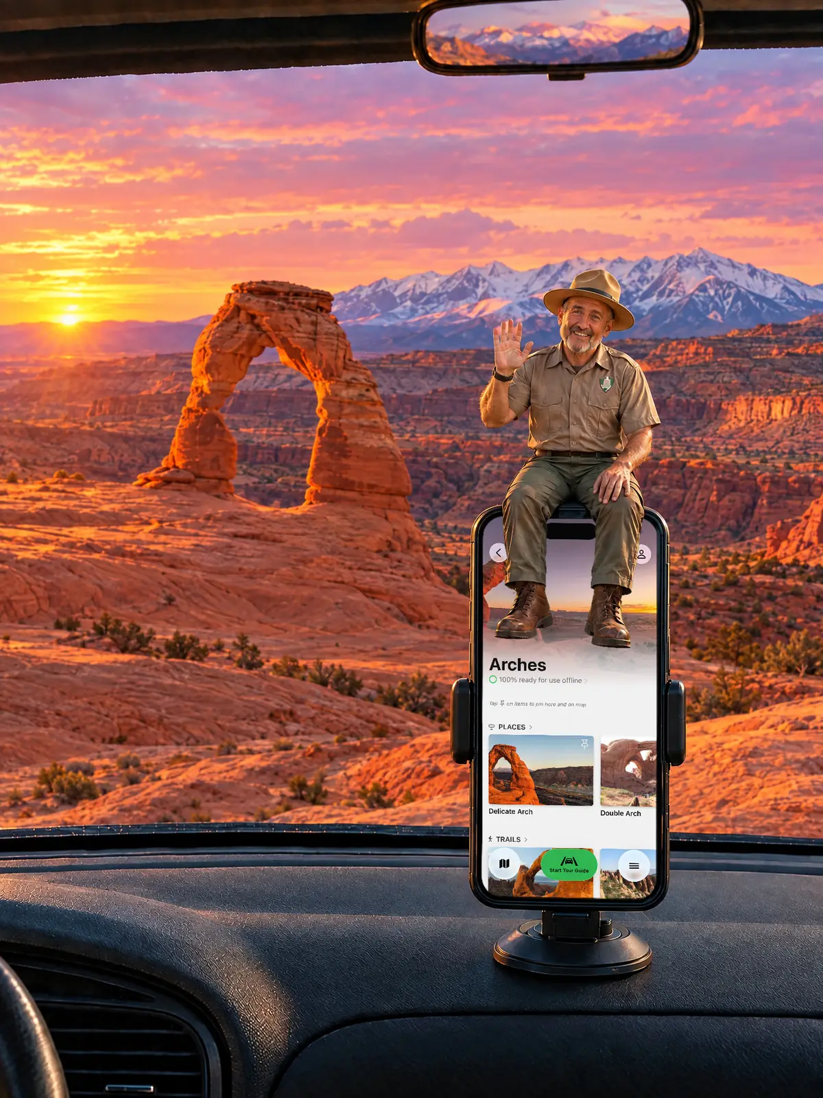 The Parkwolf tour guide waving from a dashboard phone at sunset, with Delicate Arch and the La Sal Mountains behind