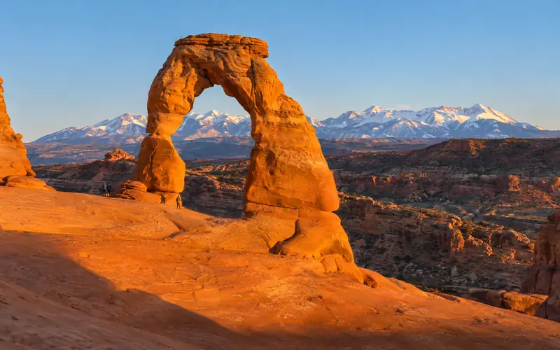 Delicate Arch glowing at golden hour with the La Sal Mountains behind it