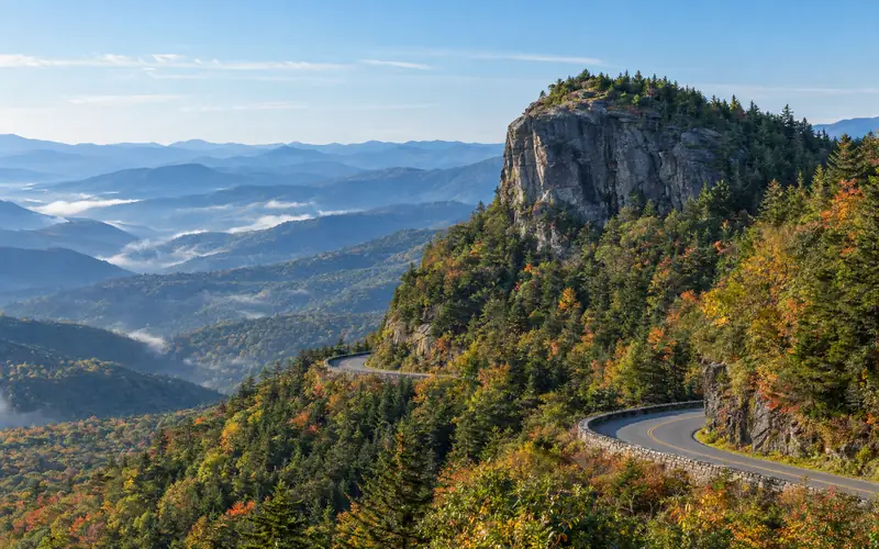 The rocky bluff of Devil's Courthouse above layered blue ridges and morning valley fog, with the Parkway curving below
