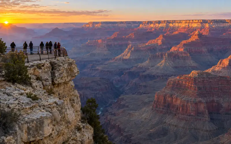 Visitors at the railing of Mather Point as the sun sits on the horizon over the Grand Canyon