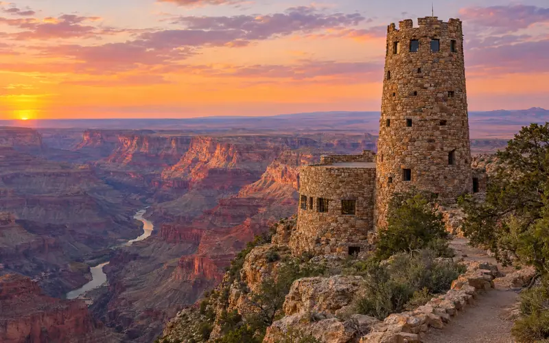 The stone Desert View Watchtower on the canyon rim at sunset, with the Colorado River below