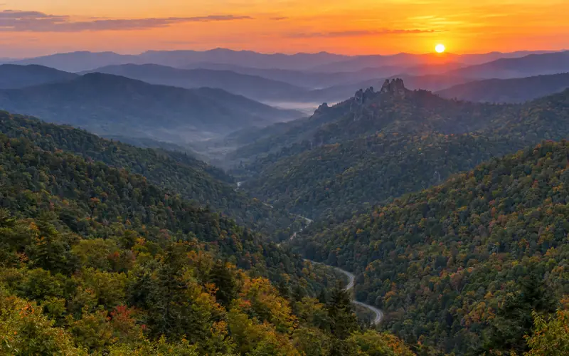 Sunset over layered blue ridges from Morton Overlook, with Newfound Gap Road winding through the valley below
